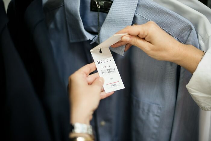 Person examining price tag on a dress shirt while shopping, highlighting cultural differences in clothing norms.