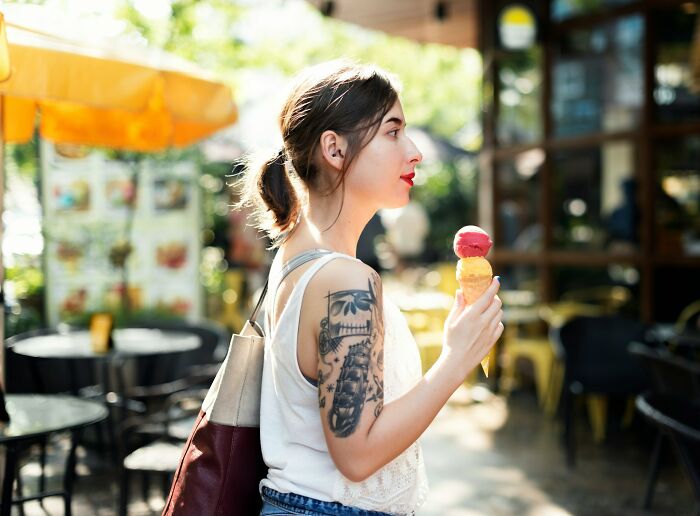 Young woman with tattoo enjoying ice cream outdoors, exemplifying amazing women confidently handling creepy advances.