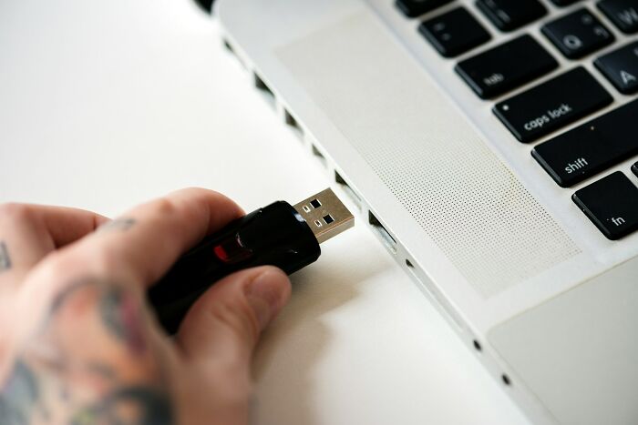 Hand with tattoo plugging USB stick into laptop, symbolizing sabotage attempts and karma consequences in digital actions.