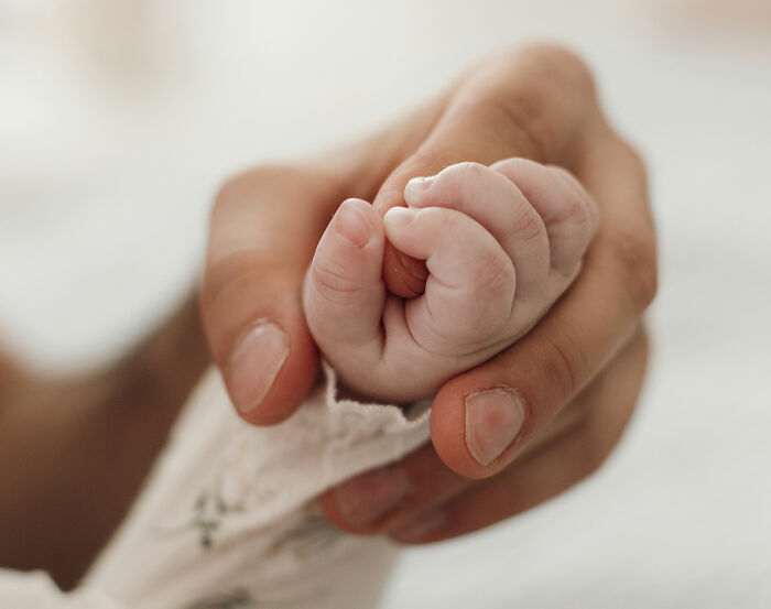 Close de uma mão adulta segurando suavemente a mão de um bebê recém-nascido, representando a conexão entre mãe e bebê em um momento delicado.