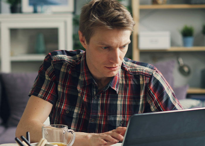 Man in a plaid shirt looking concerned while using a laptop, reflecting a friend blocked after failed love attempts.