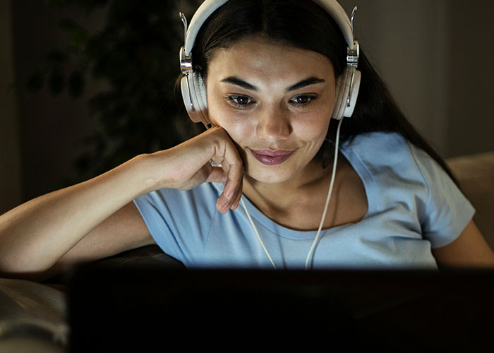 Young woman with headphones at night, smiling while trying to connect with a long-time friend online.