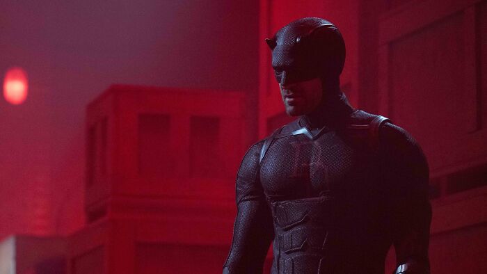 Daredevil in his black suit standing in a dimly lit red room, scene from Daredevil Born Again season 2.