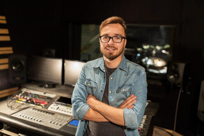 Man in a recording studio with arms crossed, showcasing dark industry secrets shared by insiders in a professional setting.