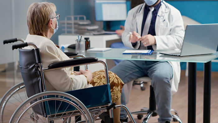 Elderly woman in wheelchair talking to a doctor in office, illustrating dark industry secrets shared by insiders.