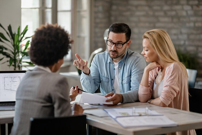 Three professionals discussing documents at a table, revealing dark industry secrets shared by insiders in a modern office.