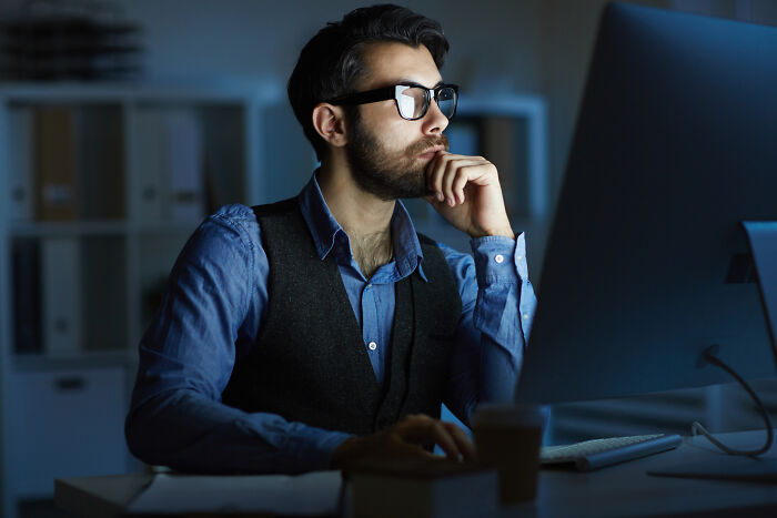 Man in glasses and vest working late on computer, contemplating dark industry secrets shared by insiders.