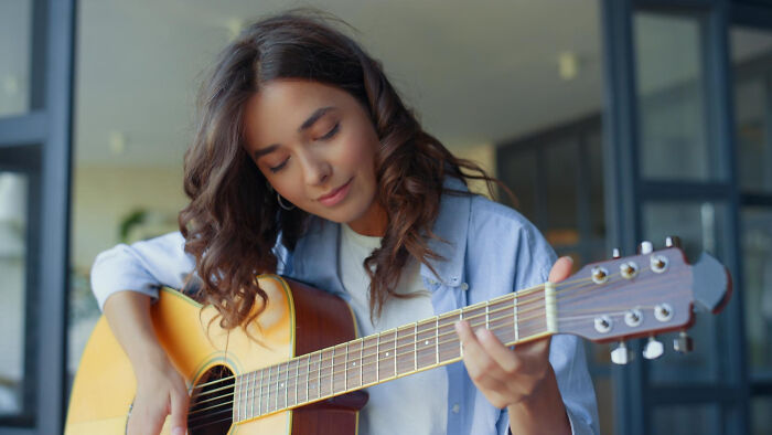 Young woman playing acoustic guitar indoors, reflecting on dark industry secrets quietly hiding behind the facade.