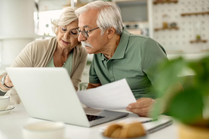Elderly couple analyzing documents and laptop screen, uncovering dark industry secrets shared by insiders in a home setting.