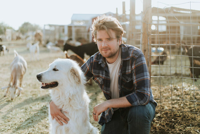 Man in a plaid shirt crouching with a large white dog on a farm, illustrating dark industry secrets shared by insiders.