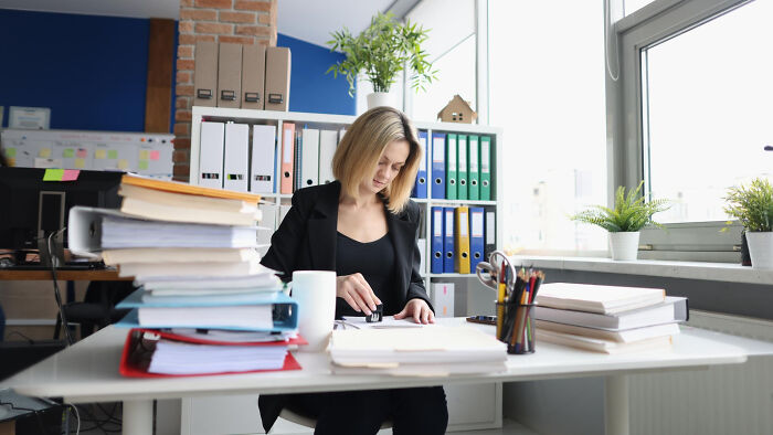 Woman working at a desk filled with paperwork, representing dark industry secrets quietly hiding behind the facade.