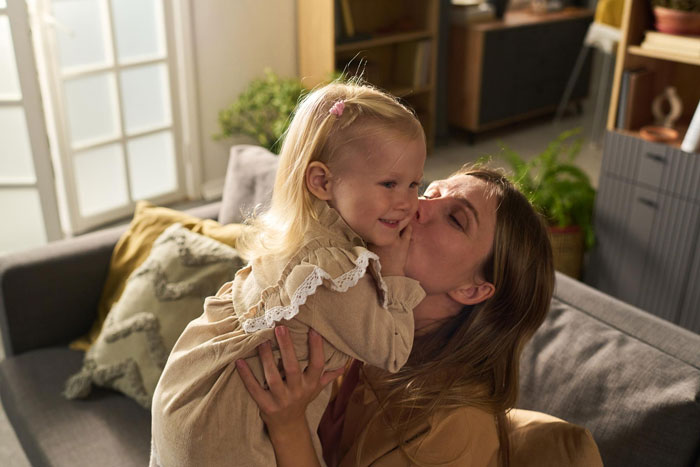 Mom holding and kissing her daughter during a small birthday celebration, reflecting the cruel dad&rsquo;s opinion on kids' birthday memories.