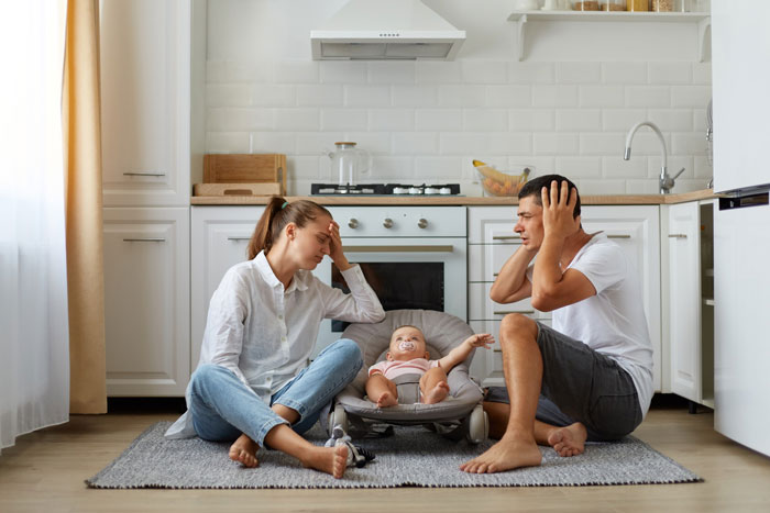 Frustrated parents sit on the floor with a baby between them, depicting family crisis and teen daughter eviction conflict.