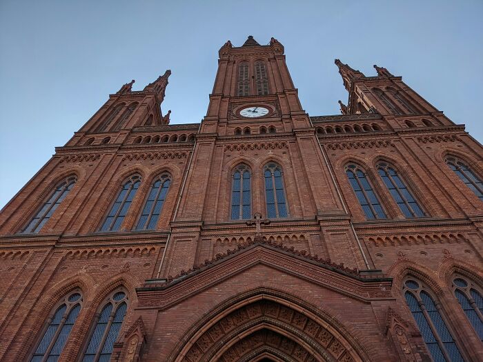 Red brick gothic-style cathedral with clock tower under clear sky, showcasing culture shock moments for foreigners.
