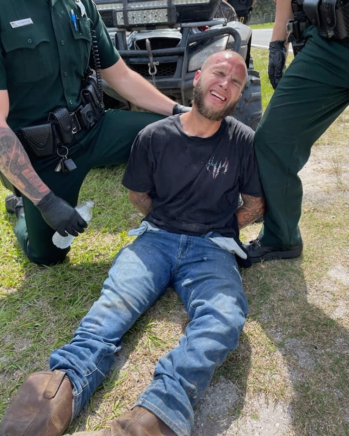 Man in black shirt handcuffed on the ground between two officers, related to mom allegedly allowing boyfriend to harm her son case