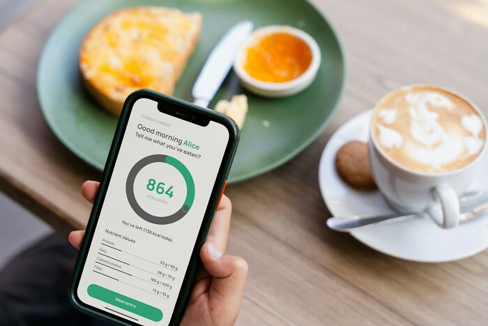 Person holding smartphone showing calorie tracking app near breakfast, representing premium-tier zombie life hacks concept.