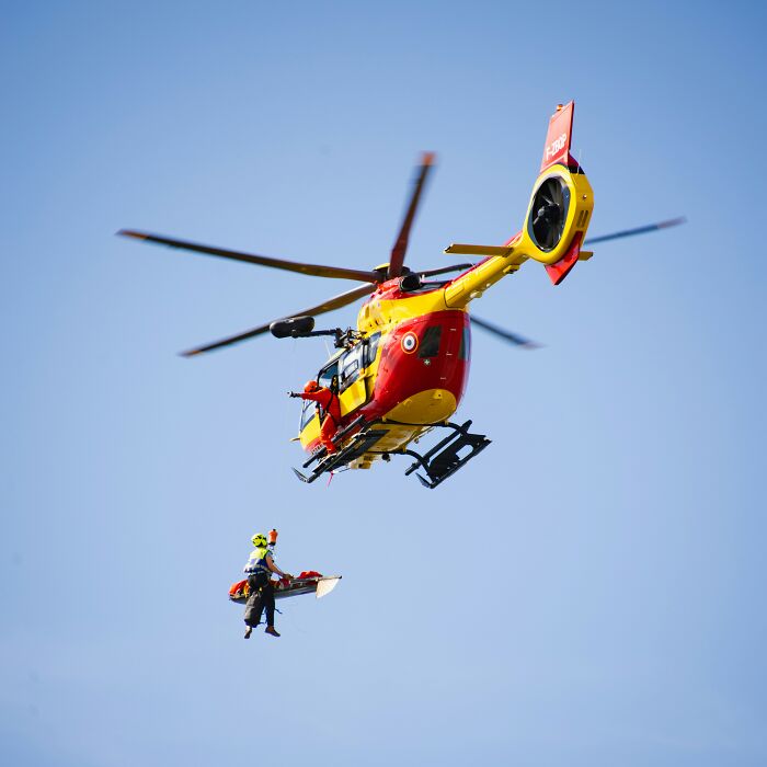 Rescue helicopter airlifting a person during a scary camping and hiking emergency in a clear blue sky.