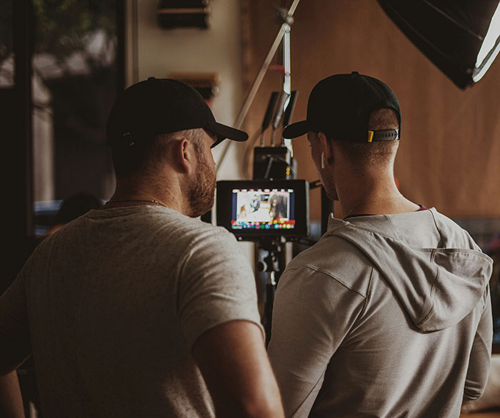 Dois membros da equipe analisam as imagens em um monitor durante as filmagens, destacando a nova abordagem de Hollywood para cenas íntimas.