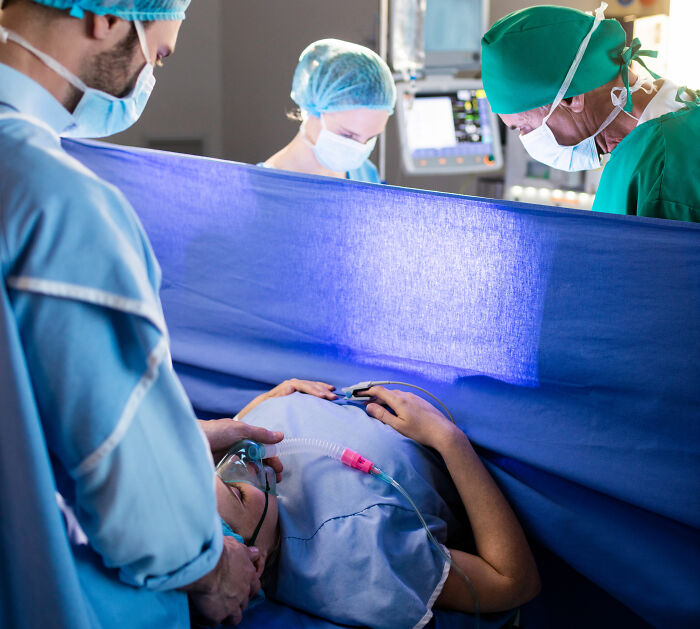 Equipe médica realizando cirurgia em paciente em sala de cirurgia, relacionado a caso de solicitação de trabalho em casa negada por mãe.