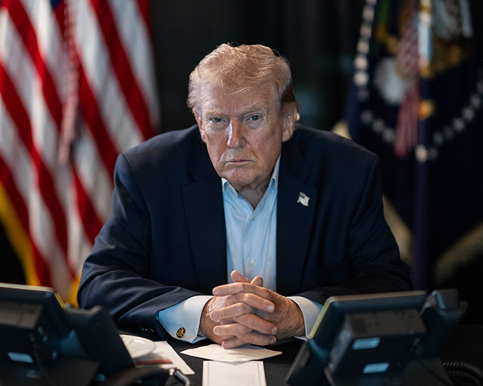 Former President Trump sitting at a desk with US flags in the background, related to doctors weighing in on neck rash.