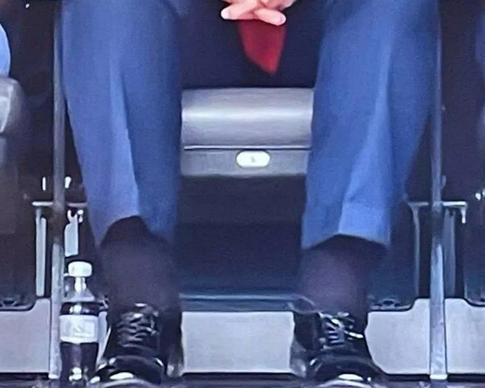 Person wearing blue pants and black shoes sitting with hands clasped, doctors weigh in on Trump&rsquo;s neck rash discussion.