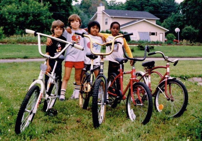 Four kids pose with their bikes in a yard, capturing a hilariously awkward childhood moment people might wish to delete.