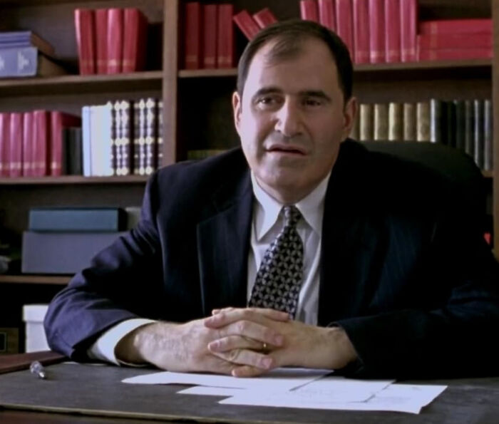 Man in suit sitting at desk with bookshelves behind, representing celebrities people used to like but now hate.