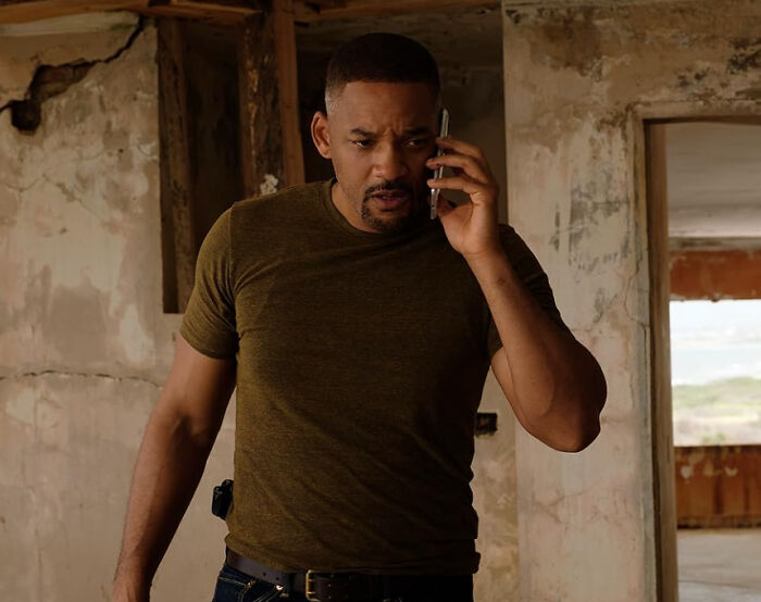 Man in a green shirt looking serious while talking on the phone in a rundown building, illustrating celebrity dislike confessions.