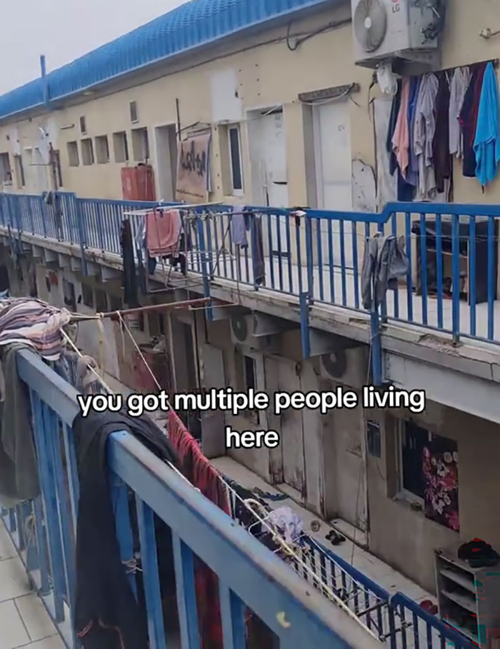 Exterior view of crowded Dubai labor camp showing clothes hanging on railings and narrow living quarters.