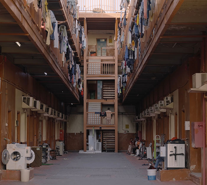 Labor camp interior in Dubai showing crowded living conditions with clothes hanging and air conditioners on walls.