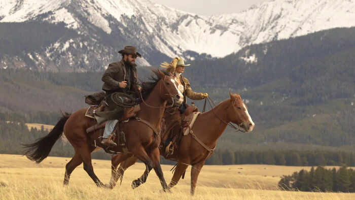 Two riders on horseback in western attire with snow-capped mountains in the background for Dutton Ranch release date.
