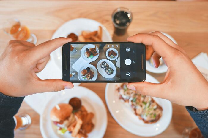 Hands holding a smartphone taking a photo of food on plates, illustrating shaky industries and consumer trends.