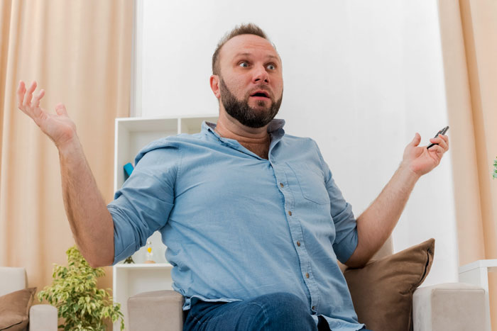 Man in blue shirt raising hands in surprise, possibly reacting to eating a bigger share at a sandwich party.