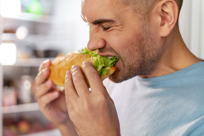 Man eating a bigger share of a sandwich at a party, enjoying fresh lettuce and bread in a casual setting