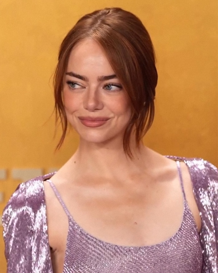 Emma Stone at the 2026 Actor Awards in a purple sequin dress, smiling and looking to the side against a gold background.