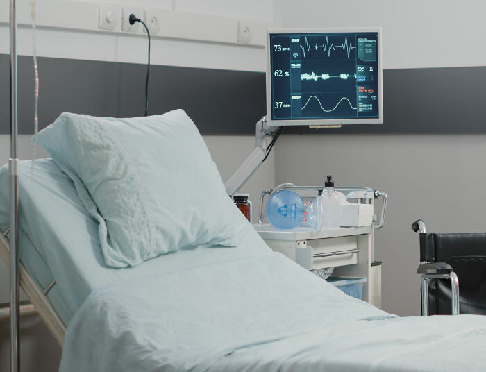 Quarto de hospital com cama vazia, monitor de frequência cardíaca e equipamento médico representando mãe indenizada por danos após solicitação de trabalho em casa negada.