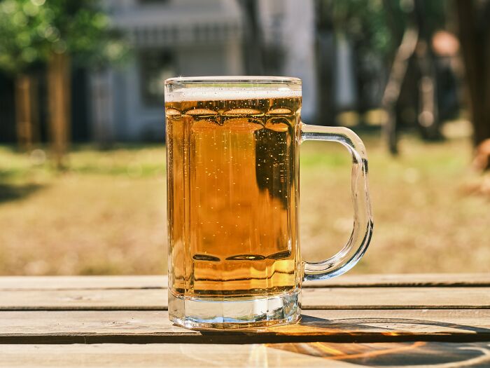 Glass mug of beer on a wooden table outdoors, illustrating cultural things people thought were normal until visiting other countries.
