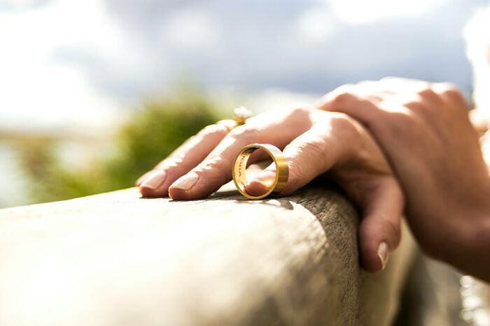 Hand with a gold ring placed on a wooden surface, symbolizing moments people destroyed their own lives in an instant.