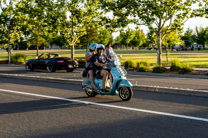 Two people riding a blue scooter on a sunny street, capturing a moment of unexpected culture shock.