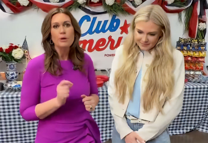 Two women standing indoors near a Club America sign, discussing Erika Kirk's latest video controversy and backlash.