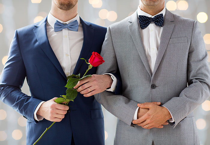 Two men in suits holding a red rose, capturing a touching moment in a love story that is gushing across the internet.