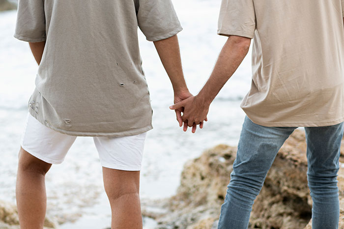 Two men holding hands near the ocean, symbolizing a heartfelt love story and emotional reconnection with an ex.