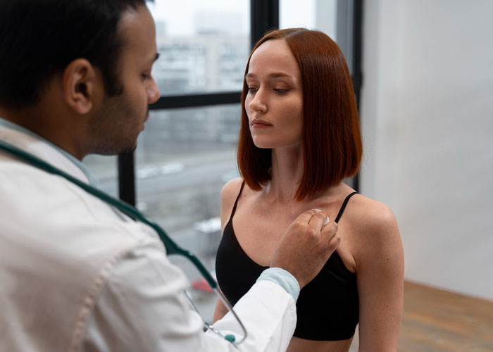 Doctor examining cancer survivor woman lifting her shirt at work to silence rumors in a clinical setting.