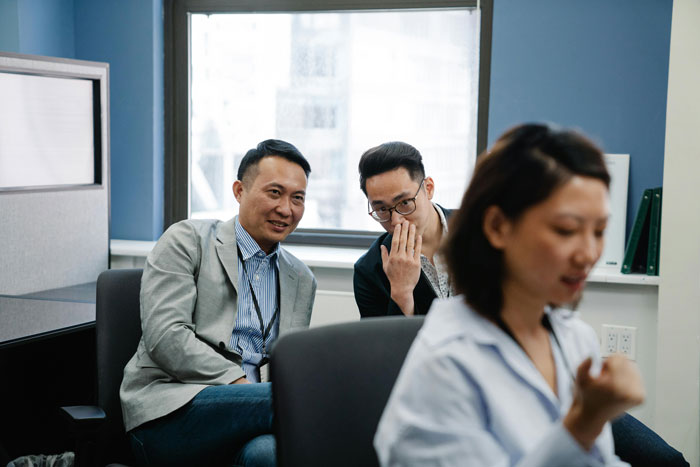 Two office workers whispering while a woman in the foreground appears worried, highlighting cancer survivor fears at work.
