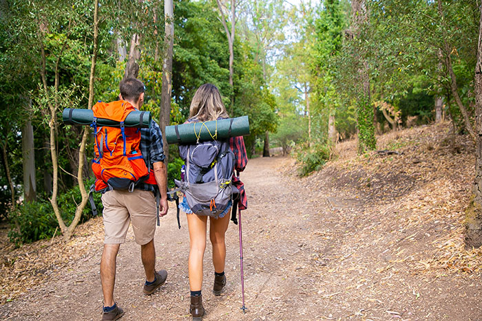 Casal caminhando ao ar livre com mochilas e equipamentos, ilustrando homens abandonando suas parceiras durante atividades ao ar livre.