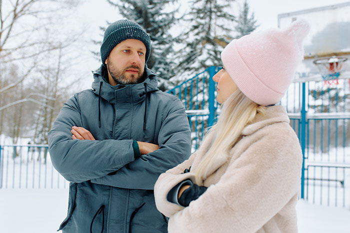 Um homem e uma mulher ao ar livre no inverno, o homem parecendo distante e desapegado durante sua atividade ao ar livre.