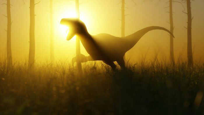 Silhouetted dinosaur running through grass at sunrise in a foggy forest, evoking a sense of mystery and age.