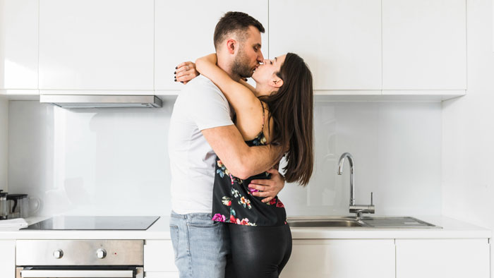 Couple embracing and kissing in a modern kitchen, illustrating emotional tension related to bride and family drama.