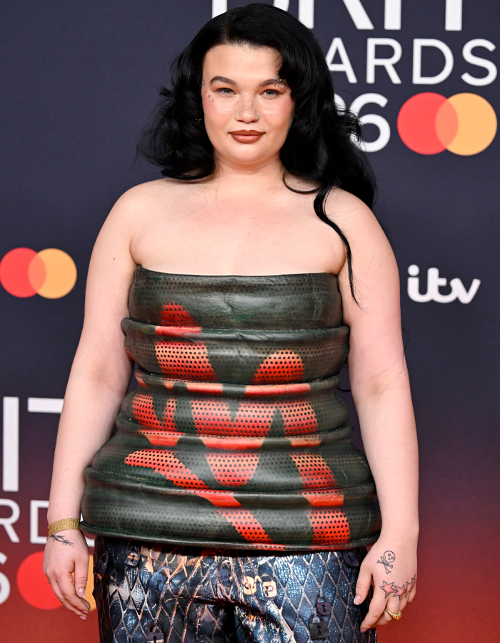Lola Young wearing a unique oil container-inspired outfit with black and red details on the Brit Awards 2026 red carpet. Lola Young wearing a unique oil container-inspired outfit with black and red details on the Brit Awards 2026 red carpet.
