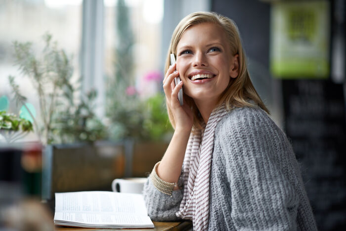 Smiling woman at cafe talking on phone, representing customers ridiculous complaints making it hard for employees to stay composed.